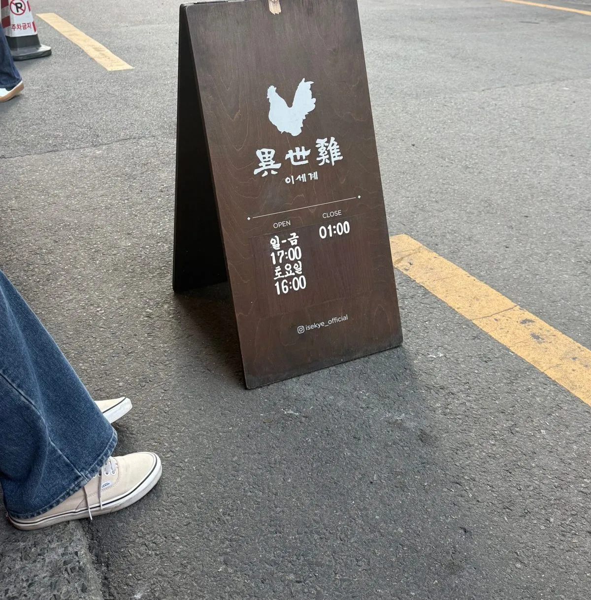길가에 세워진 이세계의 나무 입간판. 닭 그림 아래에 영업시간이 적혀 있다