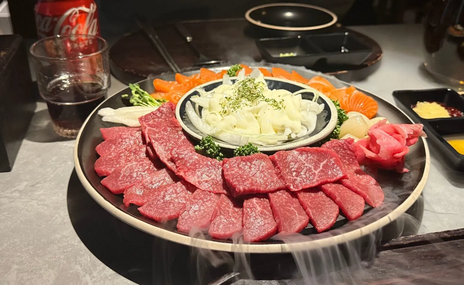 둥근 접시에 육 사시미와 연어 사시미를 담고 아래로 흰 연기가 퍼지는 모습