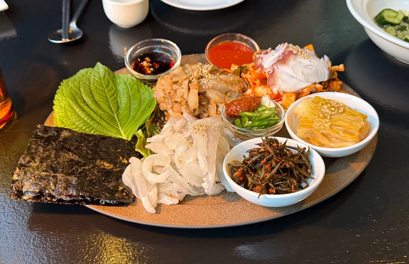 둥근 접시에 깻잎과 김, 여러 가지 곁들임을 담은 한 접시