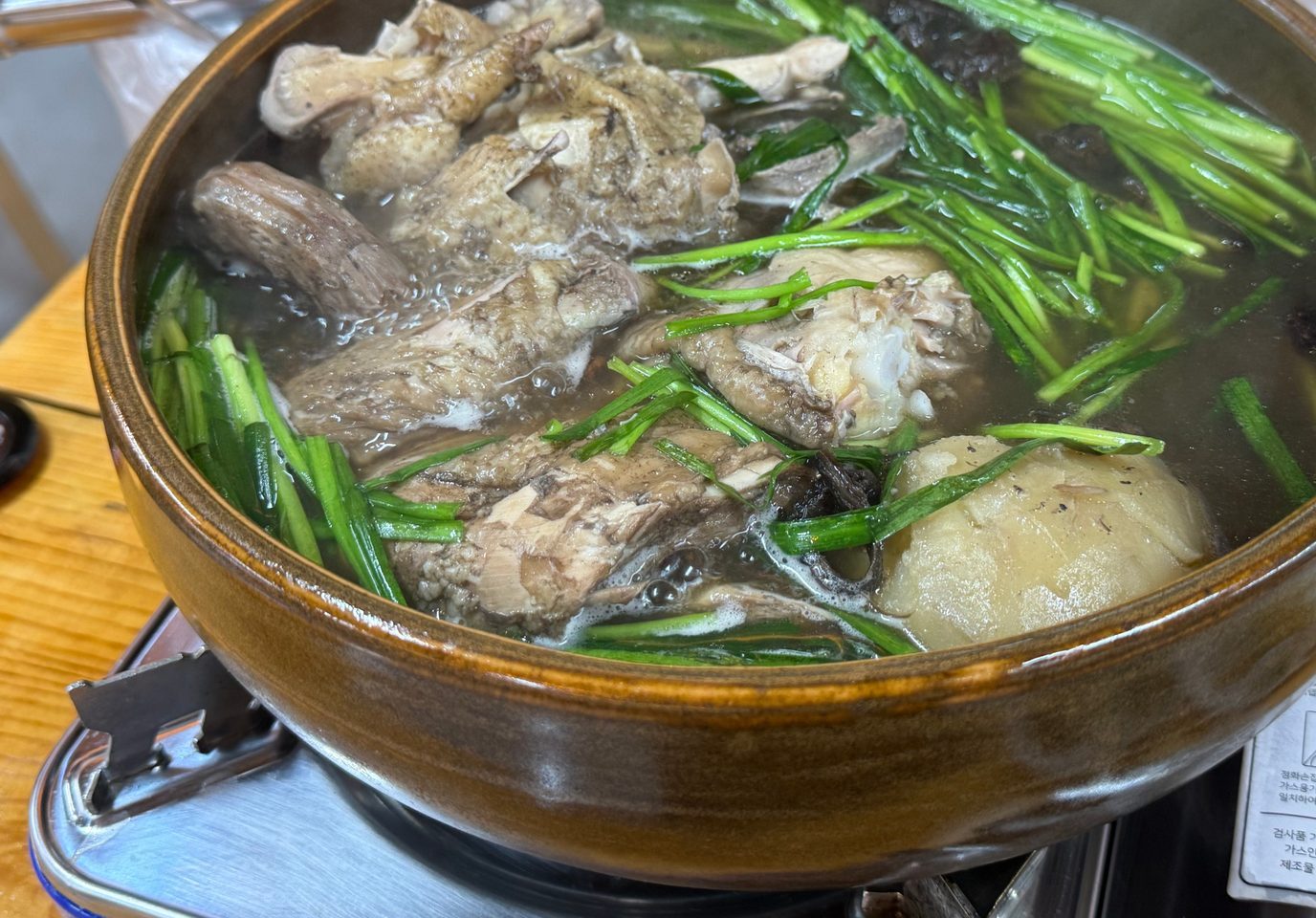 뚝배기 냄비에서 끓고 있는 토종닭백숙과 그 위에 얹은 부추와 능이버섯