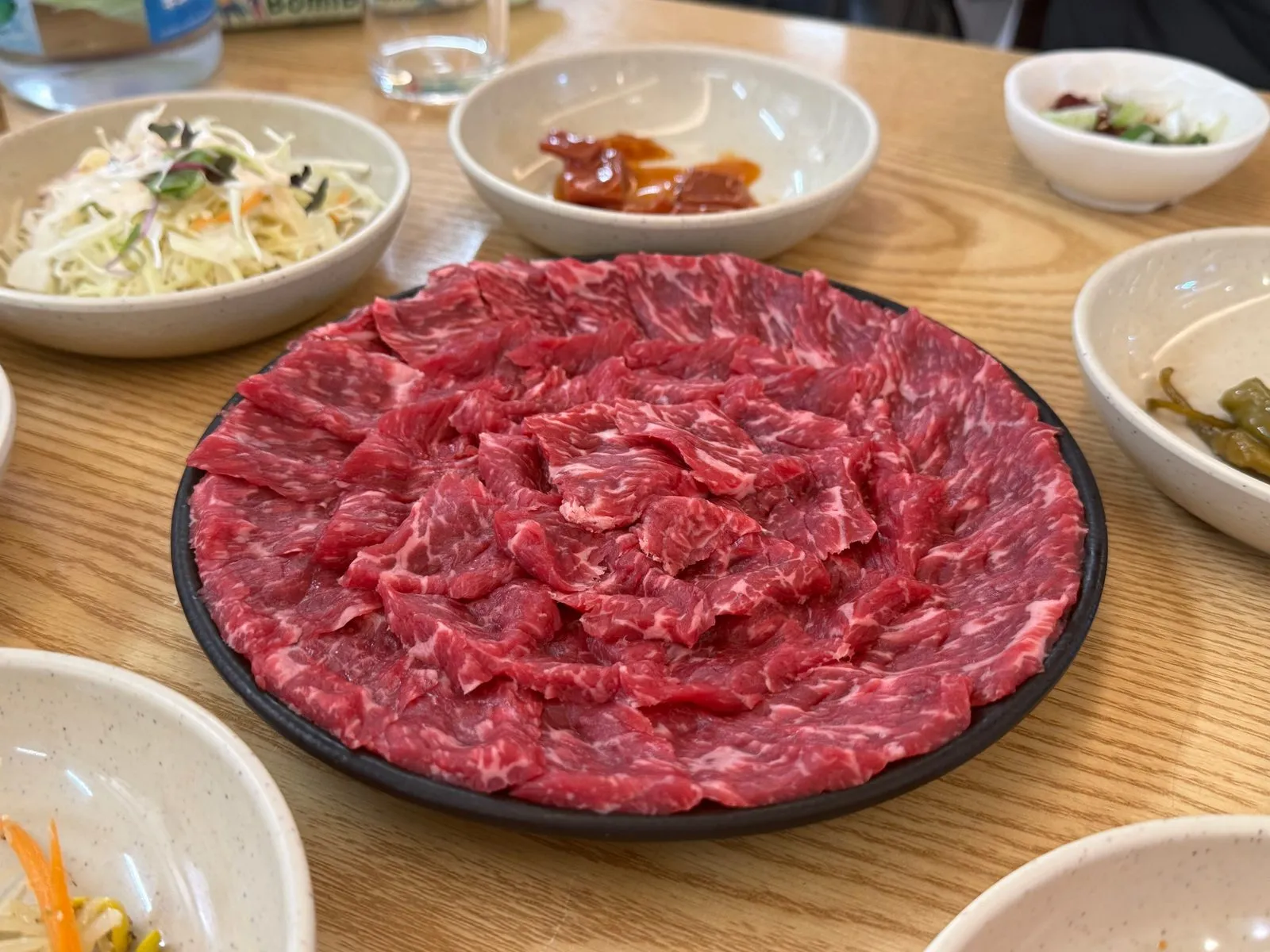 검은 접시에 넓게 펴서 담은 붉은 뭉티기와 주변의 밑반찬
