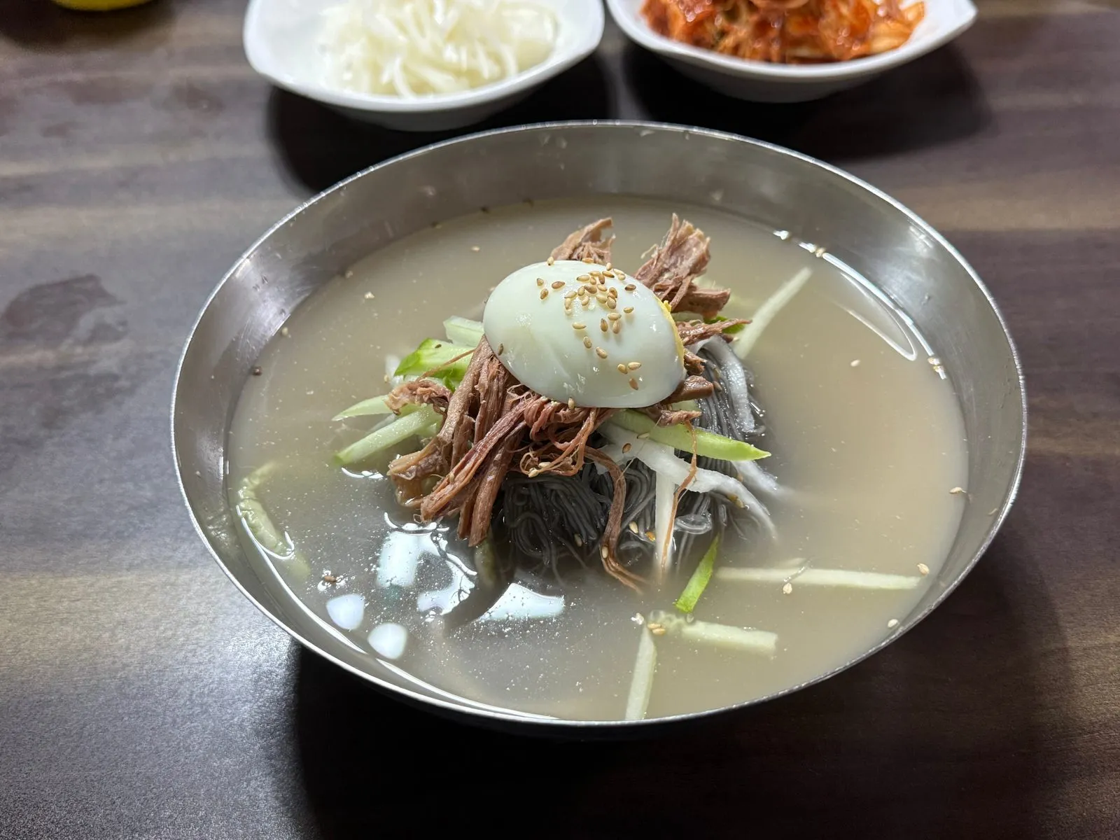 금속 그릇에 담긴 물냉면과 그 위에 올린 삶은 달걀과 고명