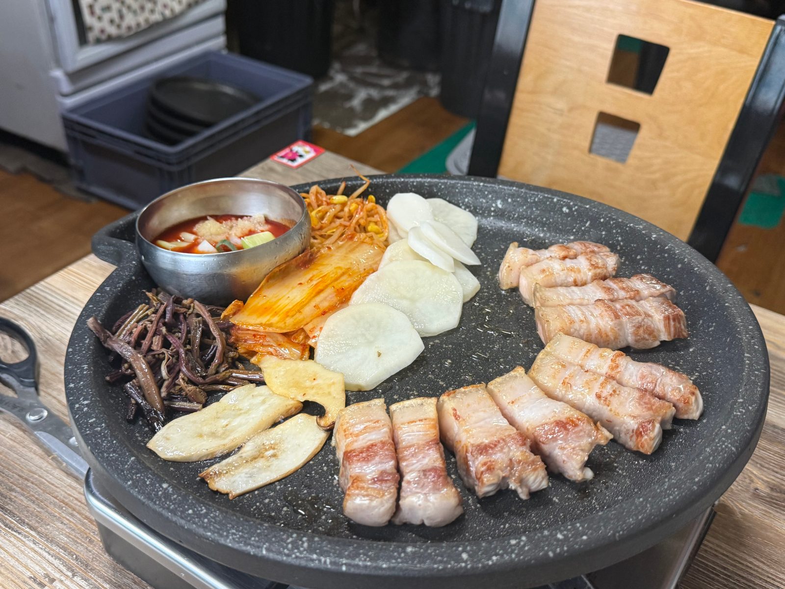 둥근 불판 위에서 익고 있는 오겹살과 김치, 버섯