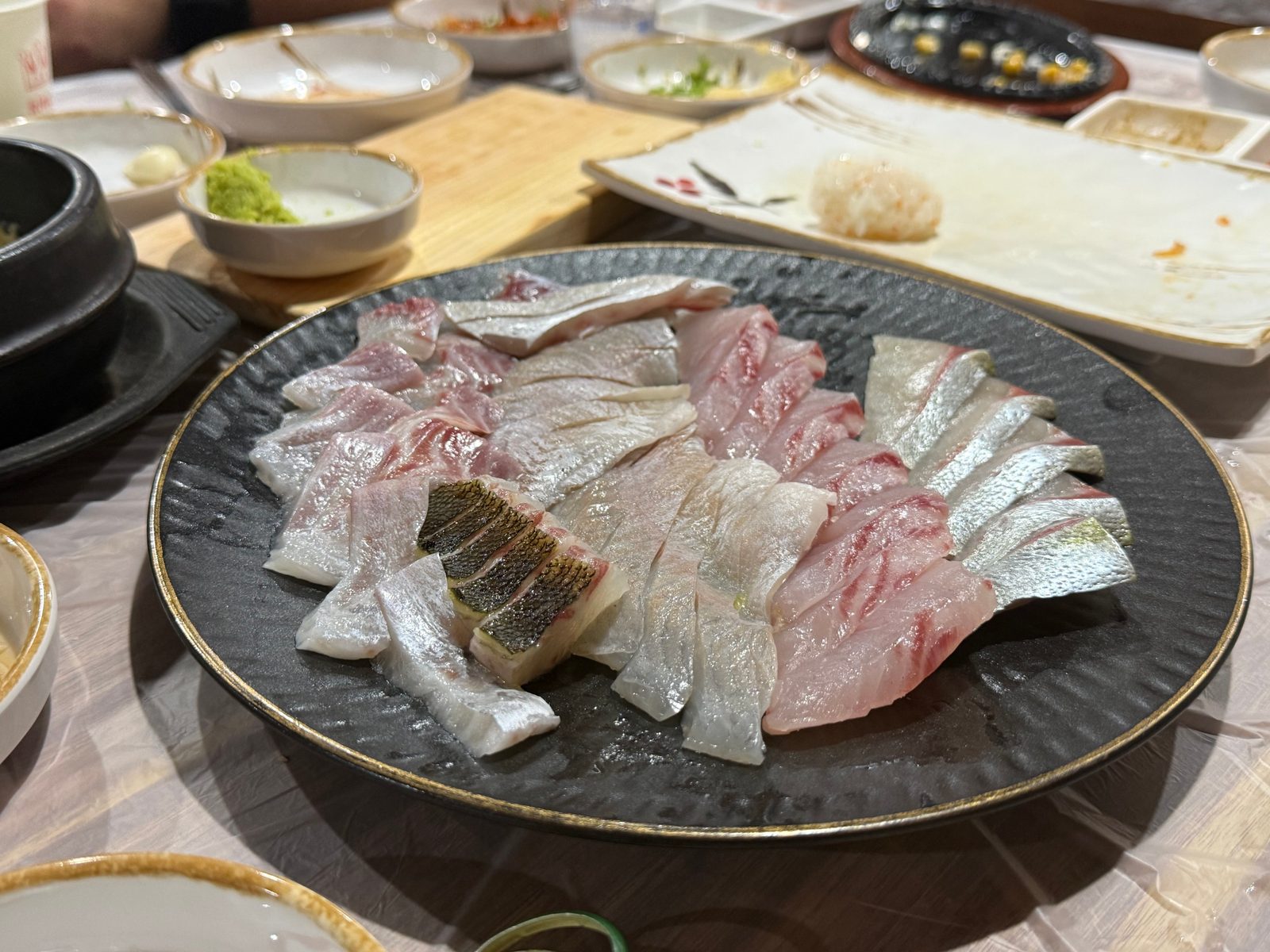 검은 접시에 여러 생선의 회를 겹쳐 담은 모습