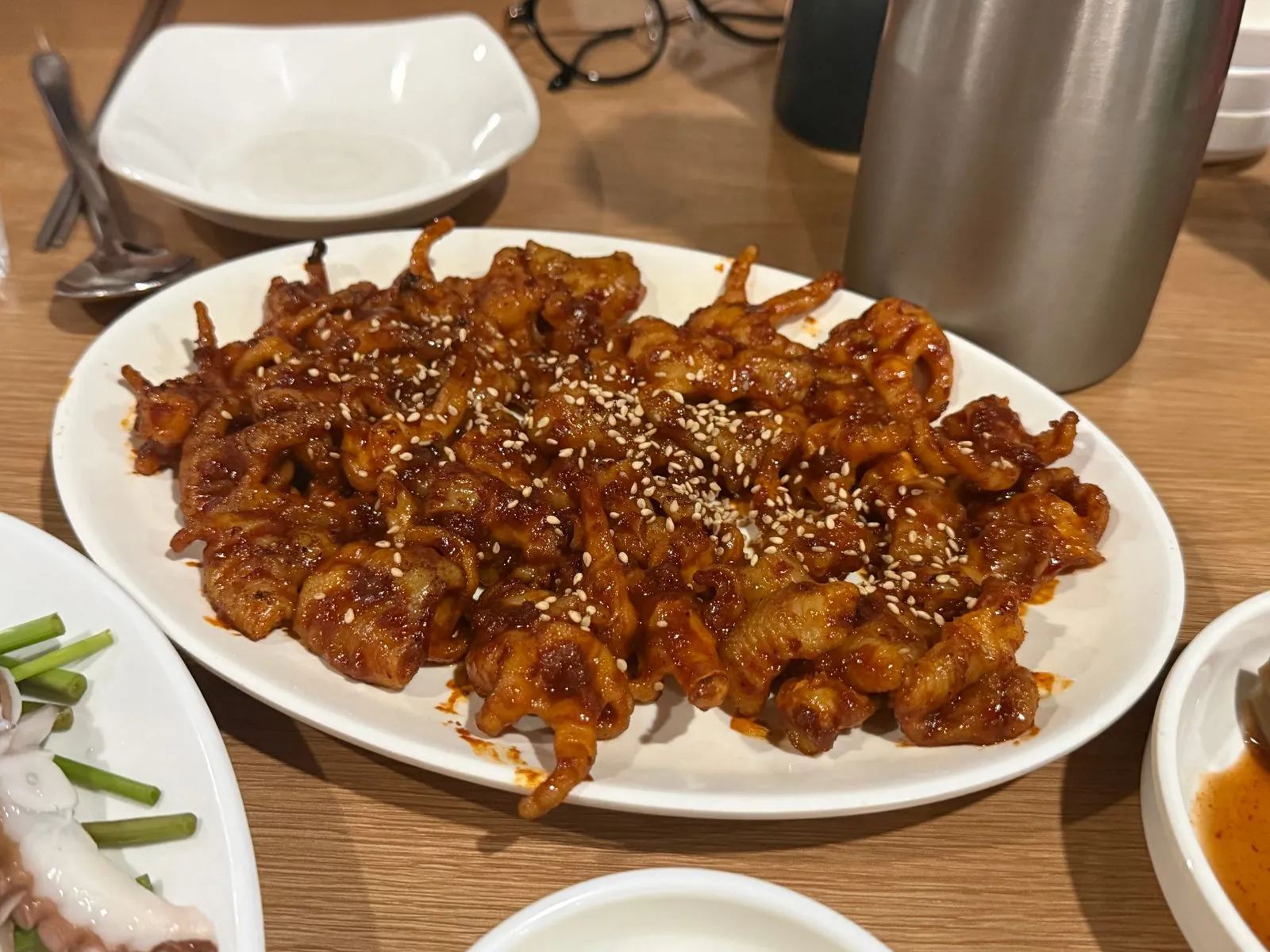 흰 접시에 담긴 양념한 뼈없는 닭발과 그 위에 뿌린 깨