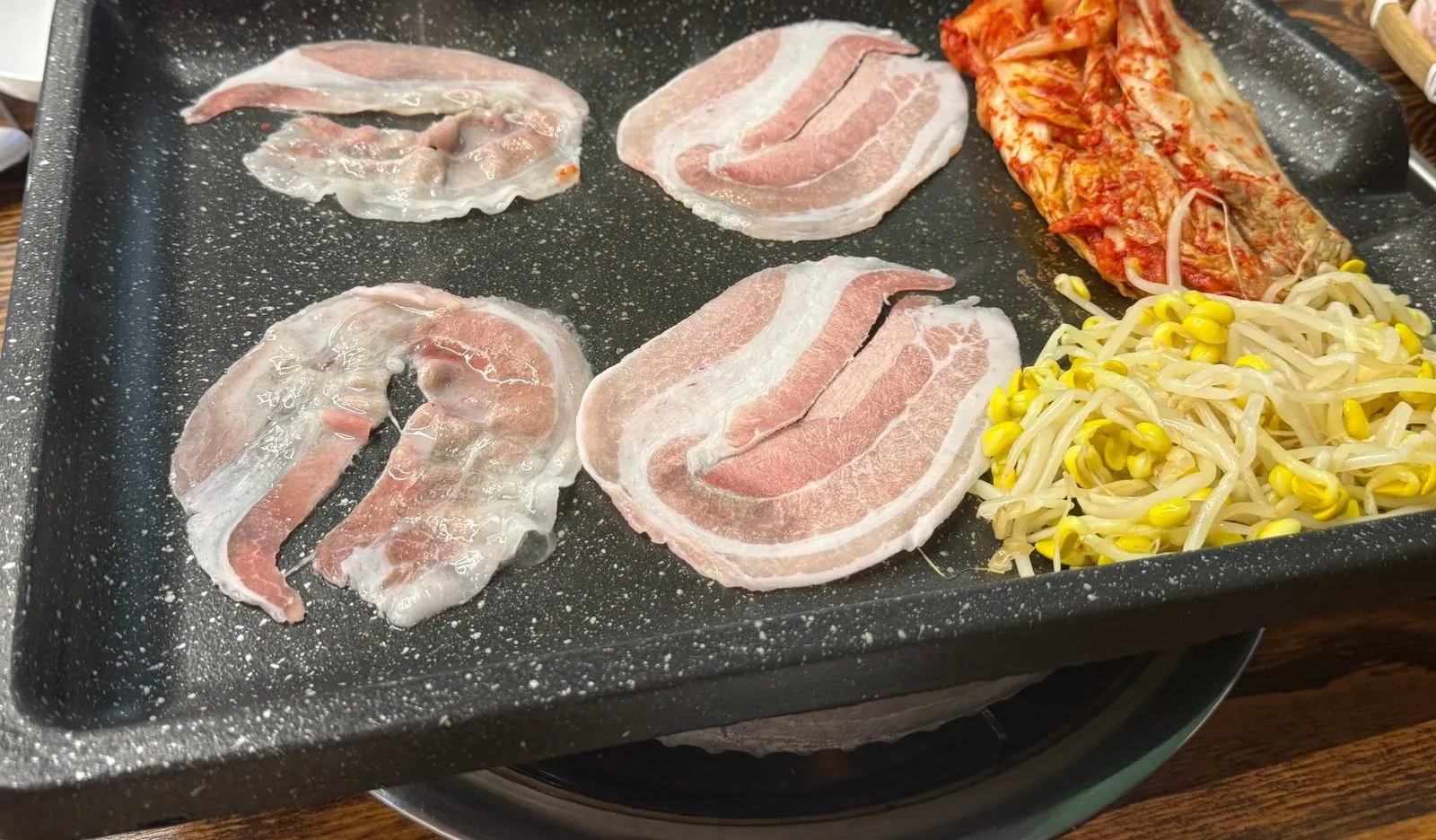 불판 위에 한 장씩 펴서 올린 삼겹살과 김치, 콩나물