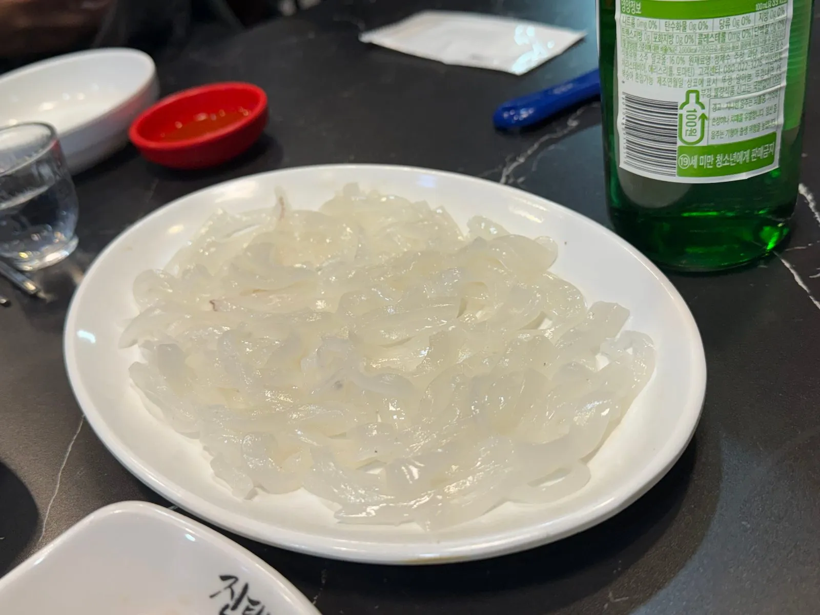 흰 접시에 얇게 썰어 담은 한치회와 소주병