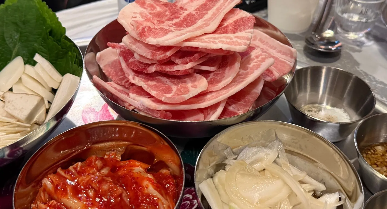 스테인리스 그릇에 겹겹이 쌓아 낸 얇은 냉동 삼겹살과 김치, 떡