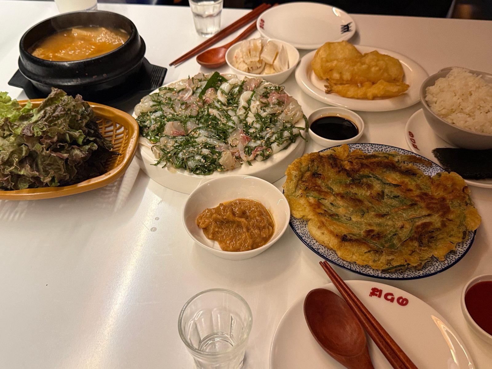 흰 상 위에 놓인 깻잎막회와 전, 쌈 채소, 찌개