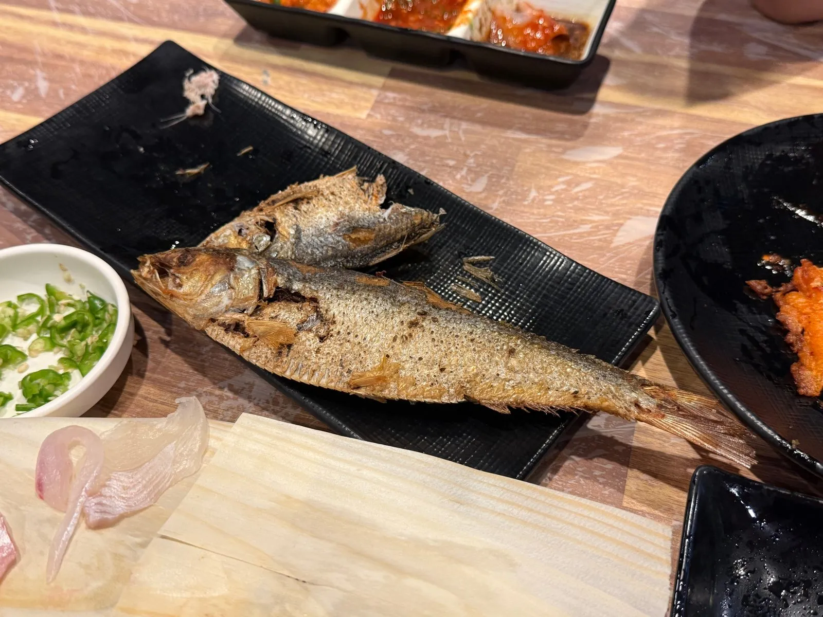 검은 접시에 놓인 통째로 구운 생선